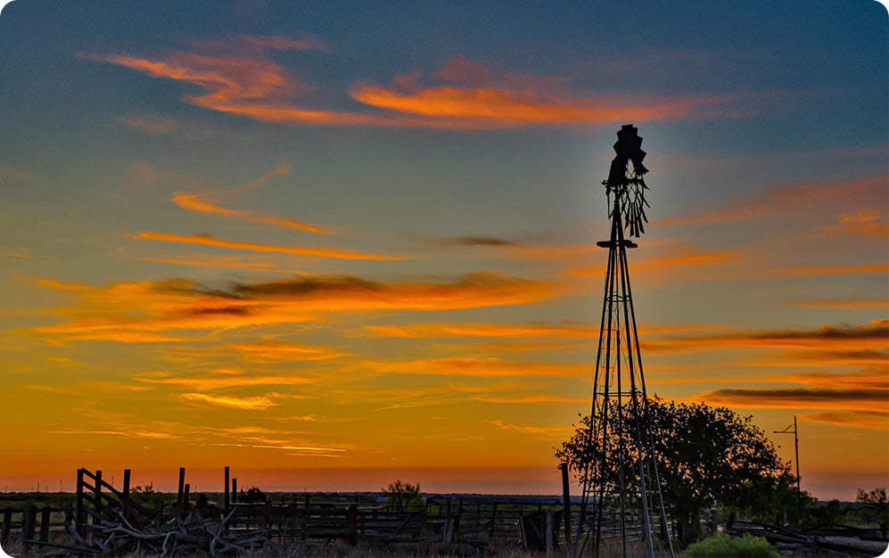 A windmill stands tall in front of a vibrant sunset, showcasing shades of orange and pink in the evening sky.
