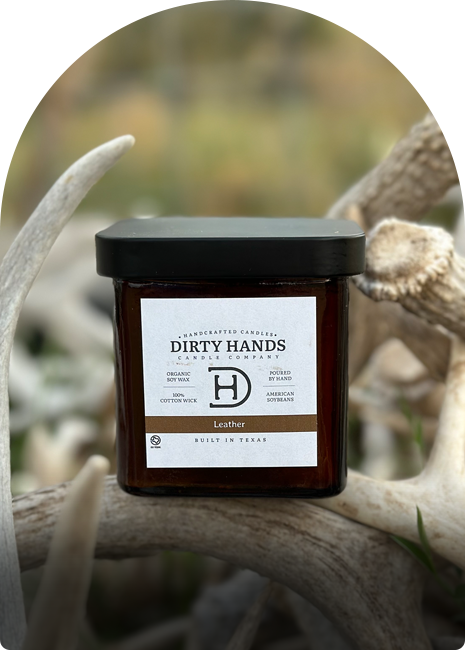 A candle is cradled by dirty hands next to deer antlers, highlighting a connection to nature and rustic decor.