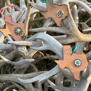 Texas-shaped leather ornaments with conchos displayed on deer antlers,this link will open in a new tab.