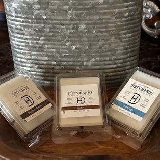 Three Dirty Hands wax melts in different scents displayed on a wooden surface, this link will open in a new tab.